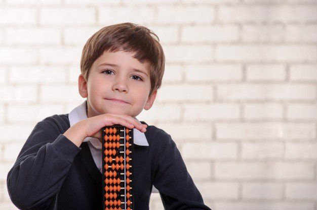 boy in school uniform holding a plus academy soroban abacus smiling