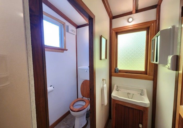 Small bathroom with toilet and sink; wooden trim; small window; neutral colors.