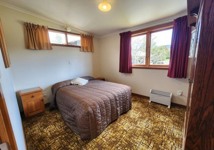 Bedroom with bed, nightstand, and window with curtains; brown and beige tones.