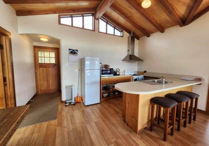 Kitchen with wood ceiling, cabinets, and flooring. A white fridge and island with stools.