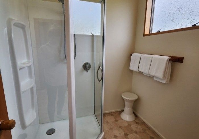 Shower stall with white walls and glass door, towels, and small stool.