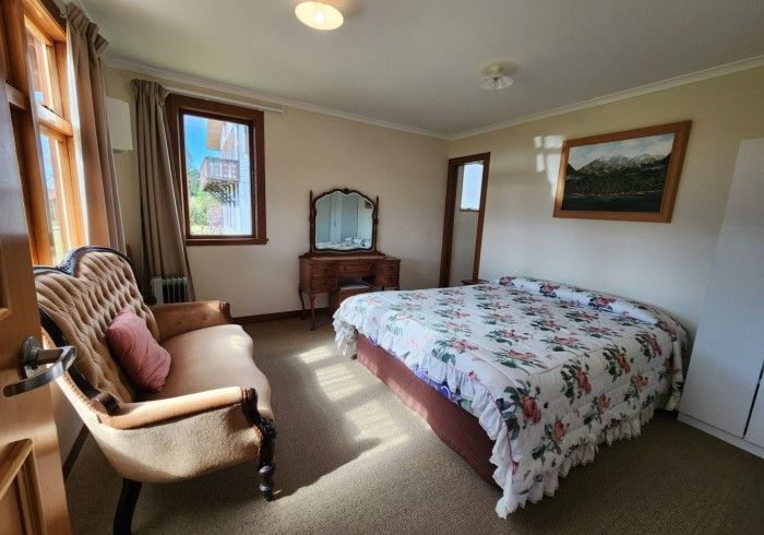 Bedroom with a bed, vanity, seating area, window, and wall art. Sunny with neutral colors.