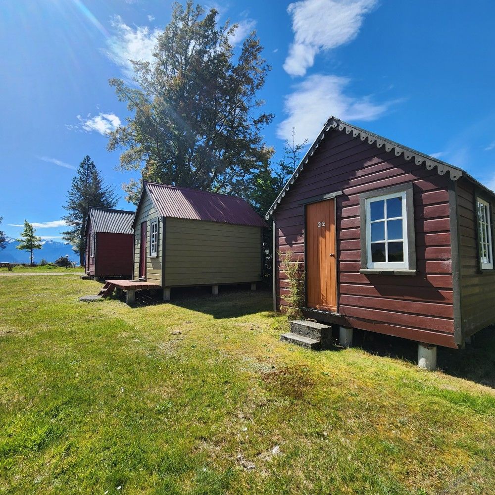 Row of small cabins on a grassy field under a blue sky, some with open doors.