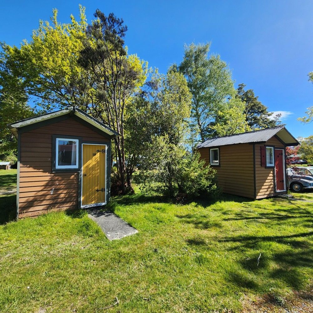 Two brown wooden sheds with different colored doors sit on a grassy lawn under a blue sky.