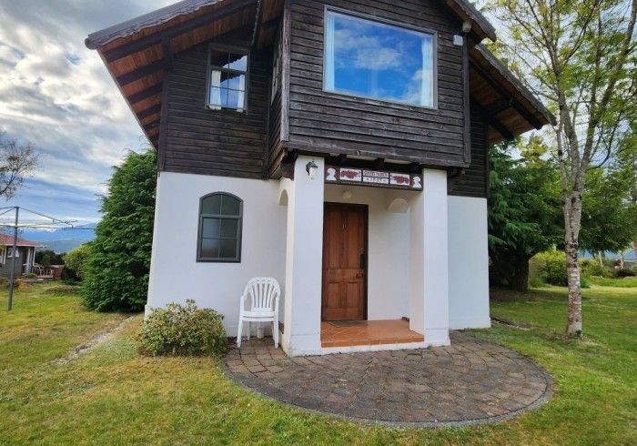 Brown cabin with white trim, arched window, and small porch; set in a grassy yard.