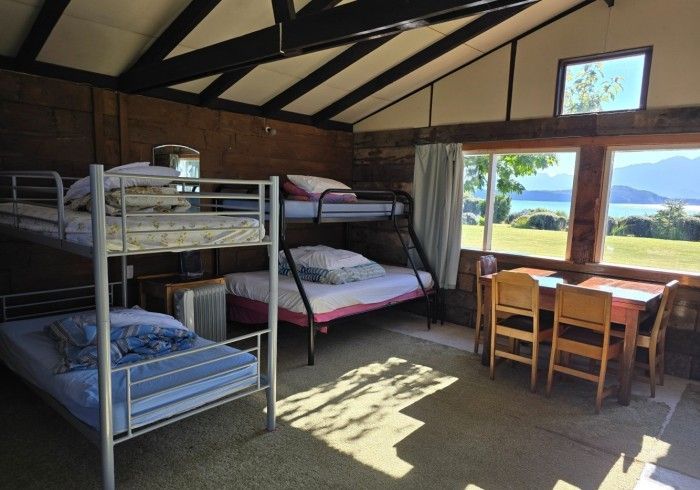 Interior of a cabin with bunk beds, a table with chairs, and windows overlooking a green landscape.
