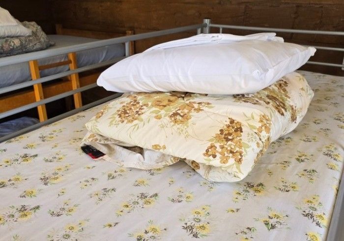 A bed with a flowered mattress, blankets, and two pillows stacked on top, inside a bunk room.