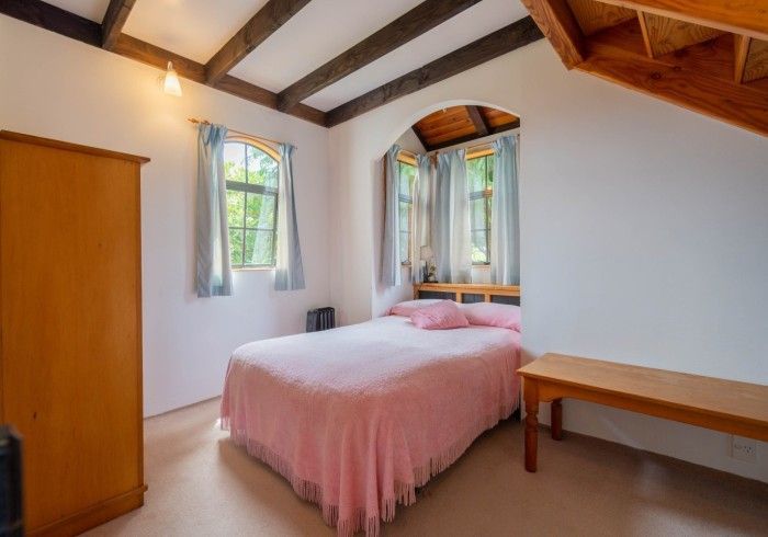 Bedroom with bed, closet, and arched windows with light blue curtains. Wooden ceiling beams.