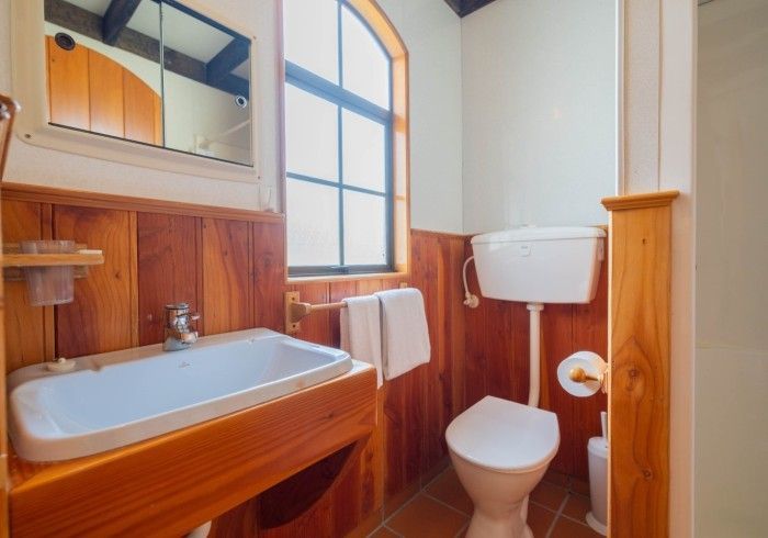 Bathroom with wood paneling, sink, toilet, window, and mirror. White and brown colors.