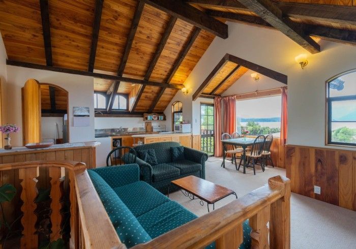 Cozy living space with wood ceiling, turquoise sofa, kitchen, dining area with lake view.