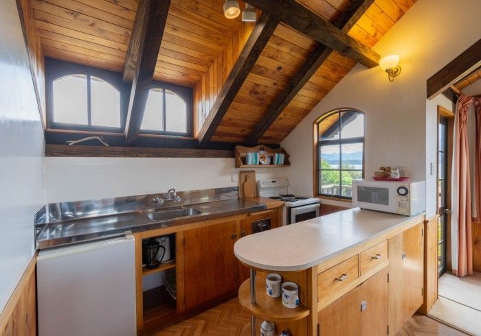 Small kitchen with wood ceiling and cabinets, stainless steel sink, microwave, and small island.
