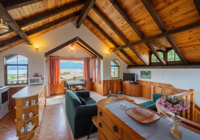 Cozy cabin interior with wooden ceiling, kitchen, living area, and a view of a lake through a window.