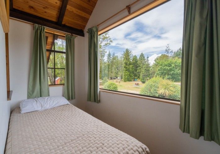 Bedroom with twin bed, green curtains, and large window overlooking trees and a meadow.