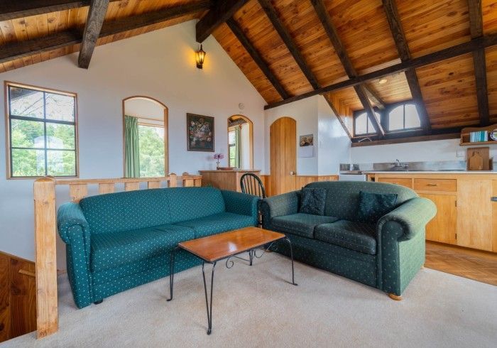 Living room with green couches, wooden ceiling, windows, and a small table.