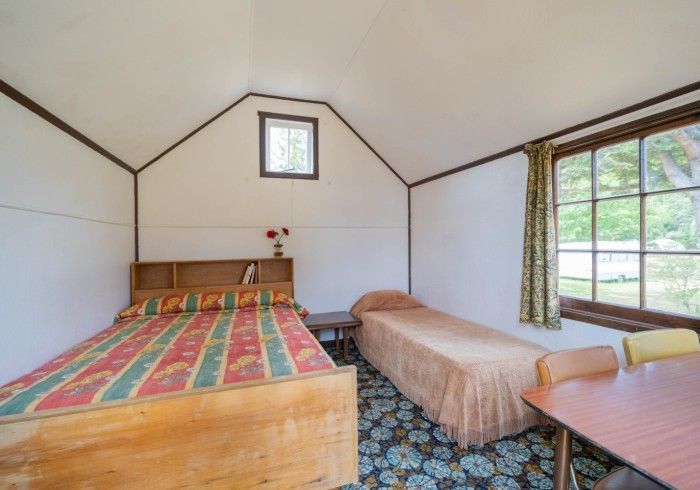 Small, rustic bedroom with two beds, small window, and a table.