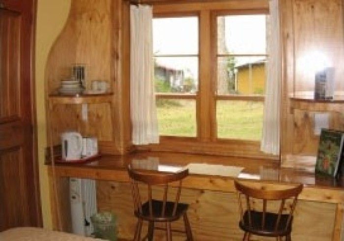 Wooden desk with chairs in front of a window, shelves with dishes and books.