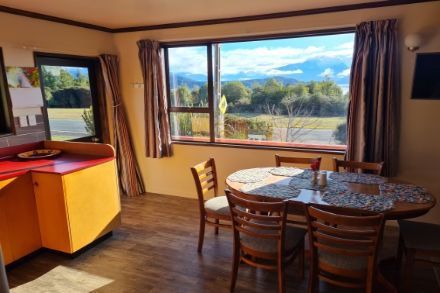 Dining area with a round table and chairs, a large window with a view of mountains and fields.