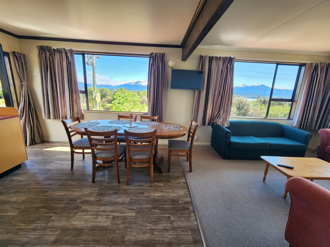 Living room with dining table, sofa, and mountain views through windows.