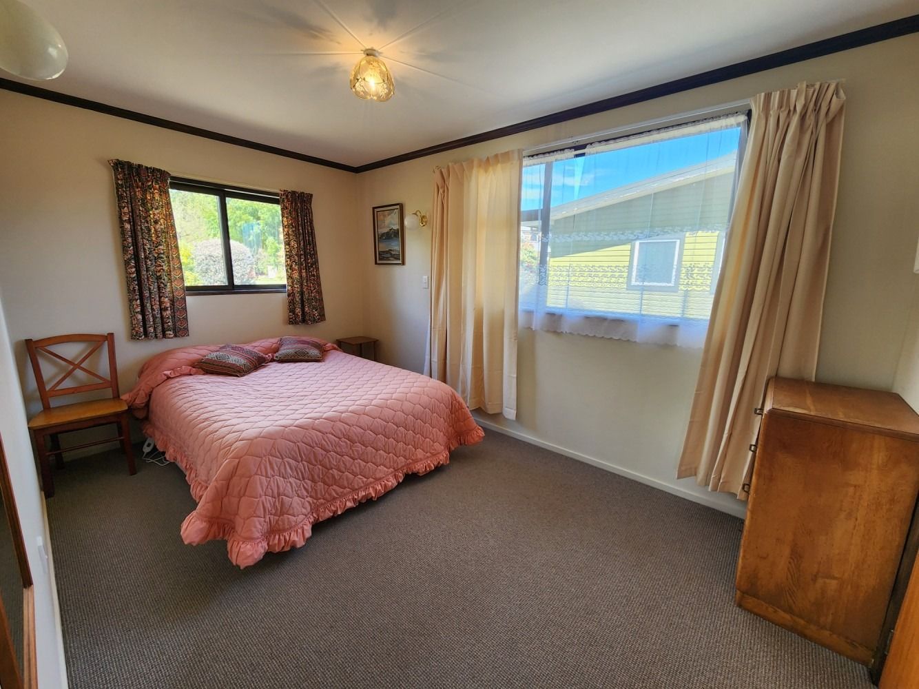 Bedroom with a bed, windows with curtains, and a wooden dresser.