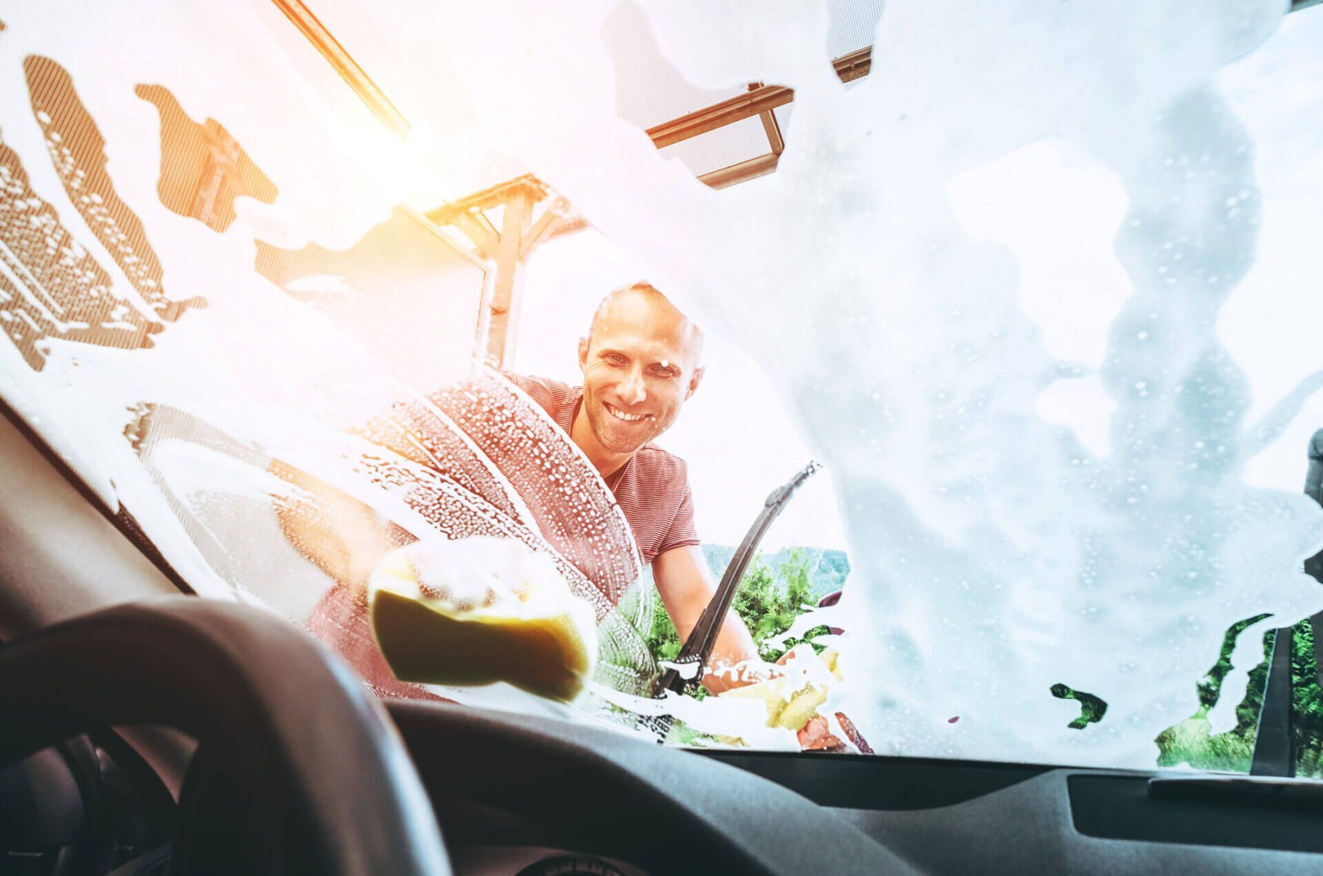 A man is washing the windshield of his car with a sponge.