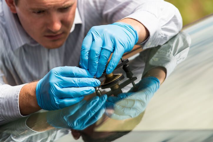 A man wearing blue gloves is repairing a windshield on a car.