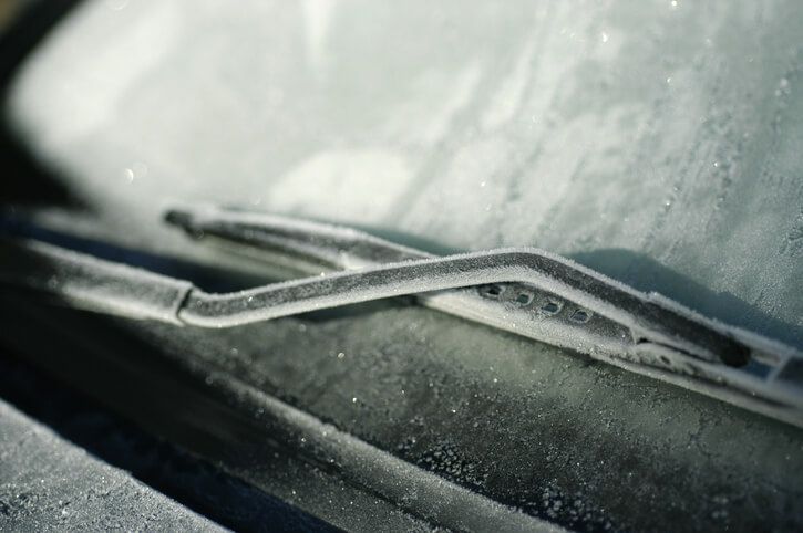 A close up of a windshield wiper on a car covered in snow.
