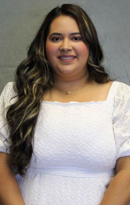 Woman with long wavy hair in white dress smiles at camera.