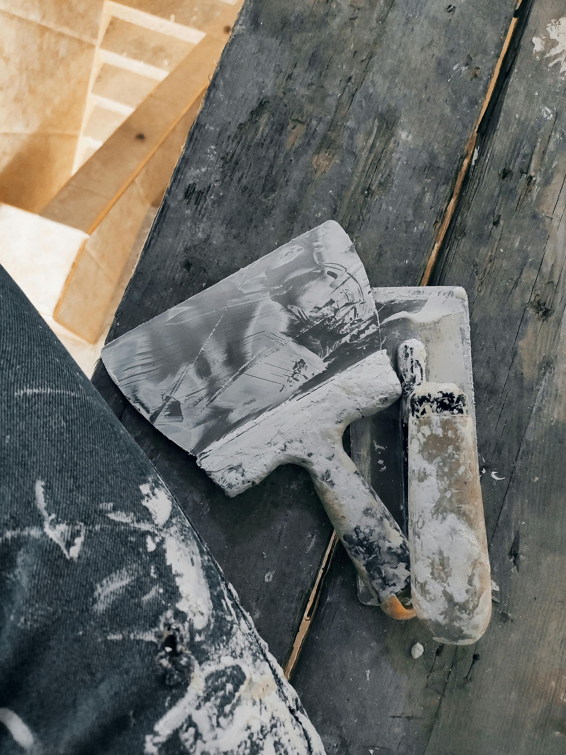 Two putty knives covered in compound on a wooden surface.