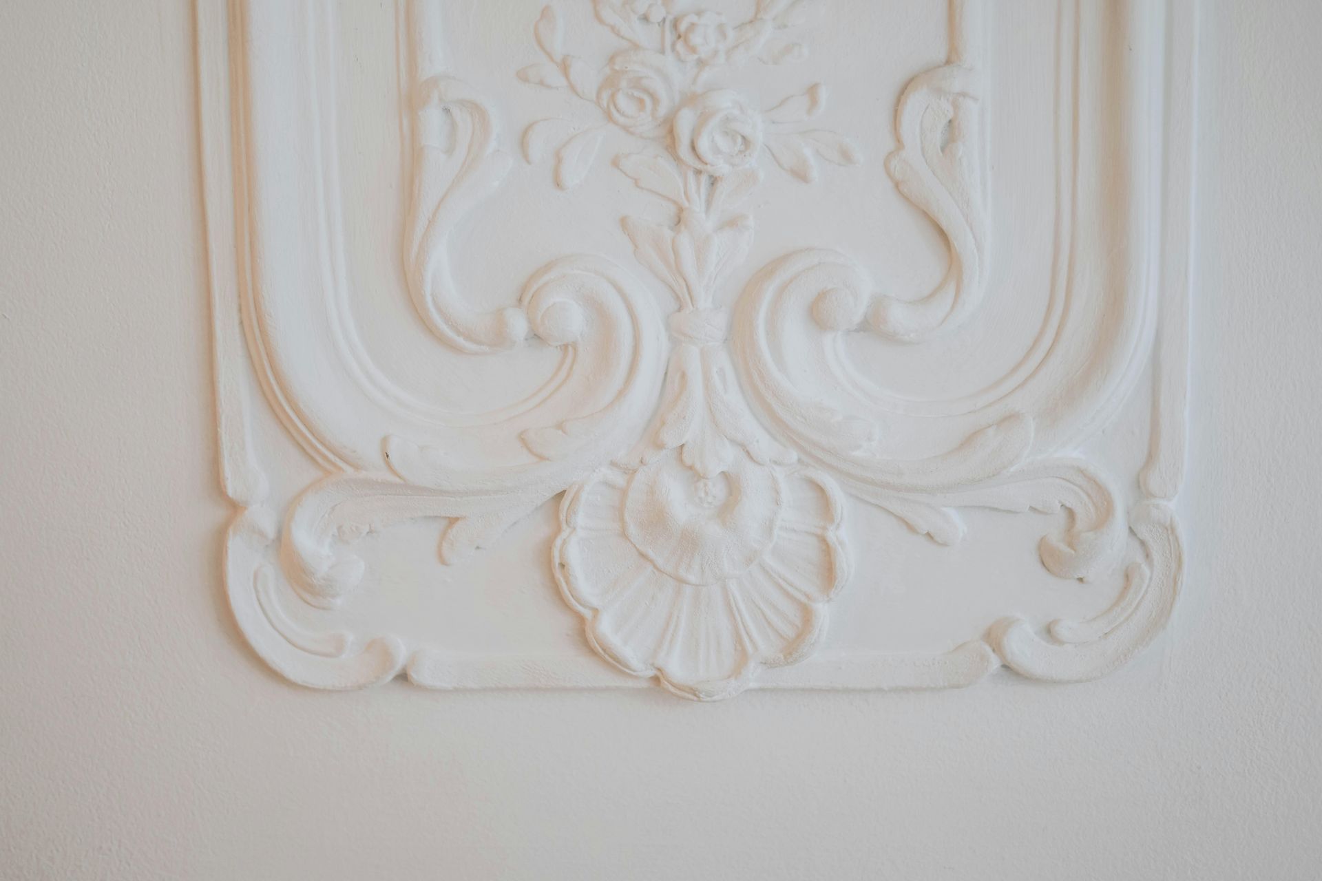 White plaster wall molding with ornate floral and scroll designs.