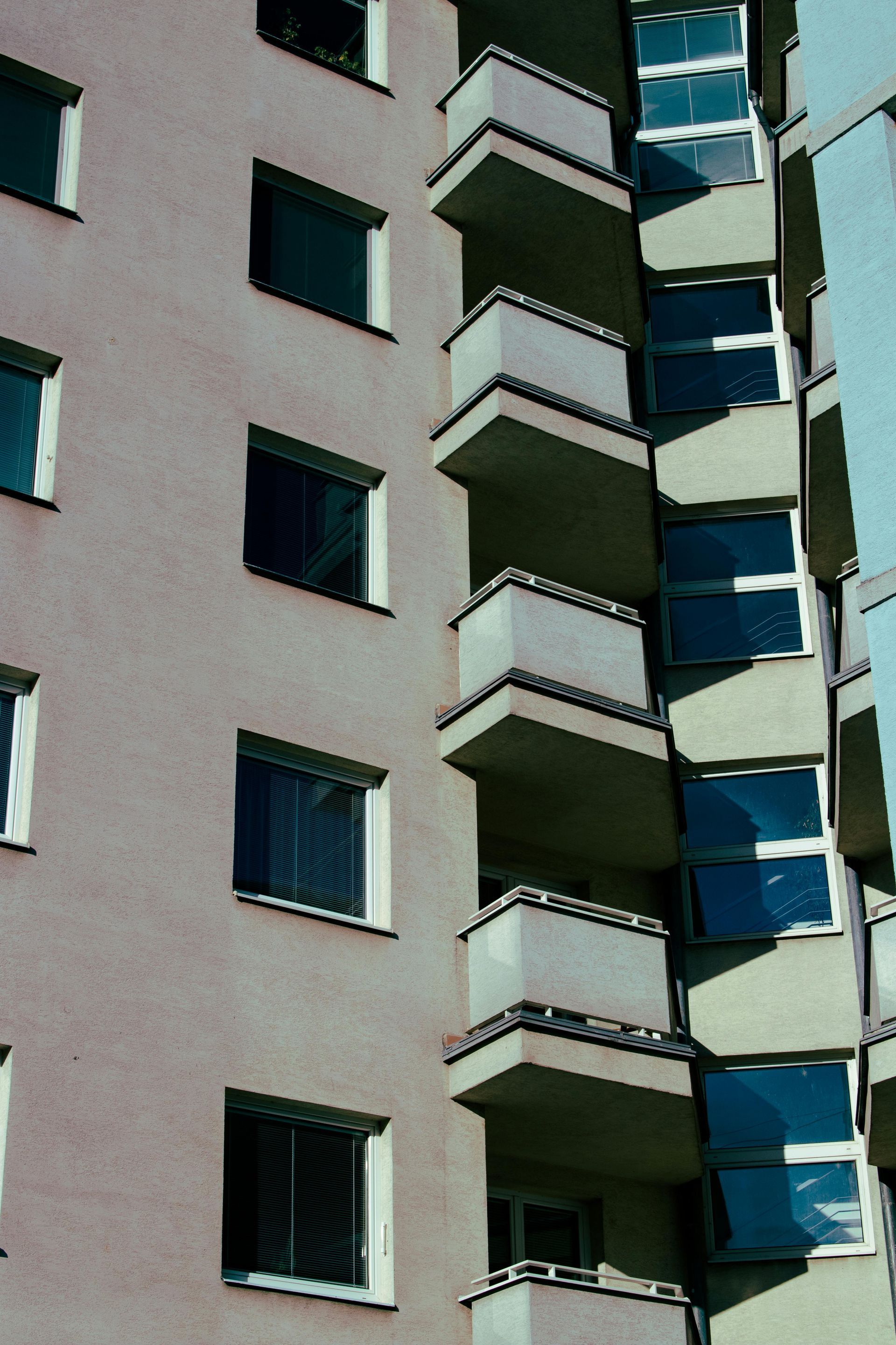 Tall apartment building with balconies and windows, the windows reflecting the sky.