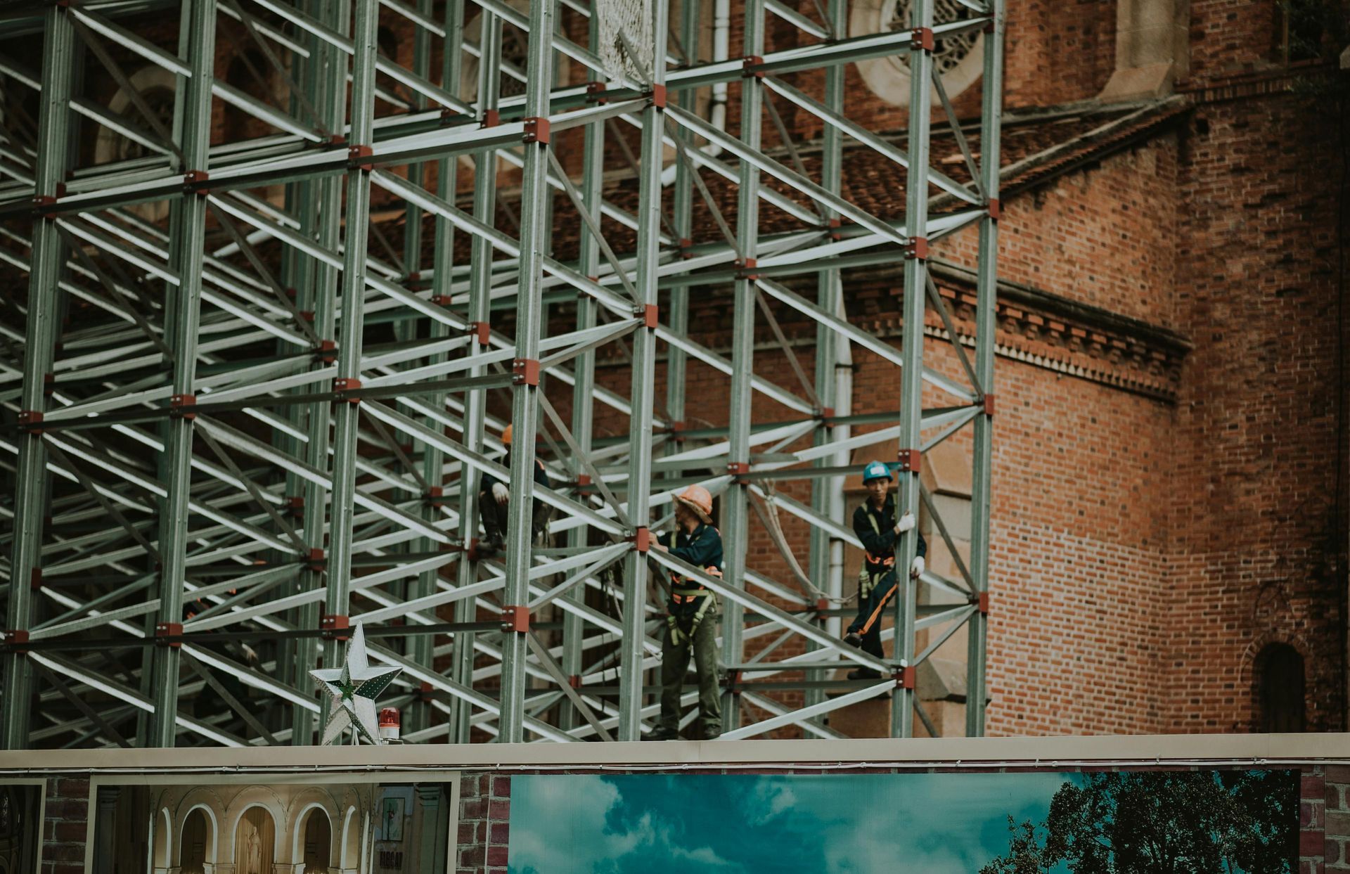 Workers on metal scaffolding in front of a brick building.
