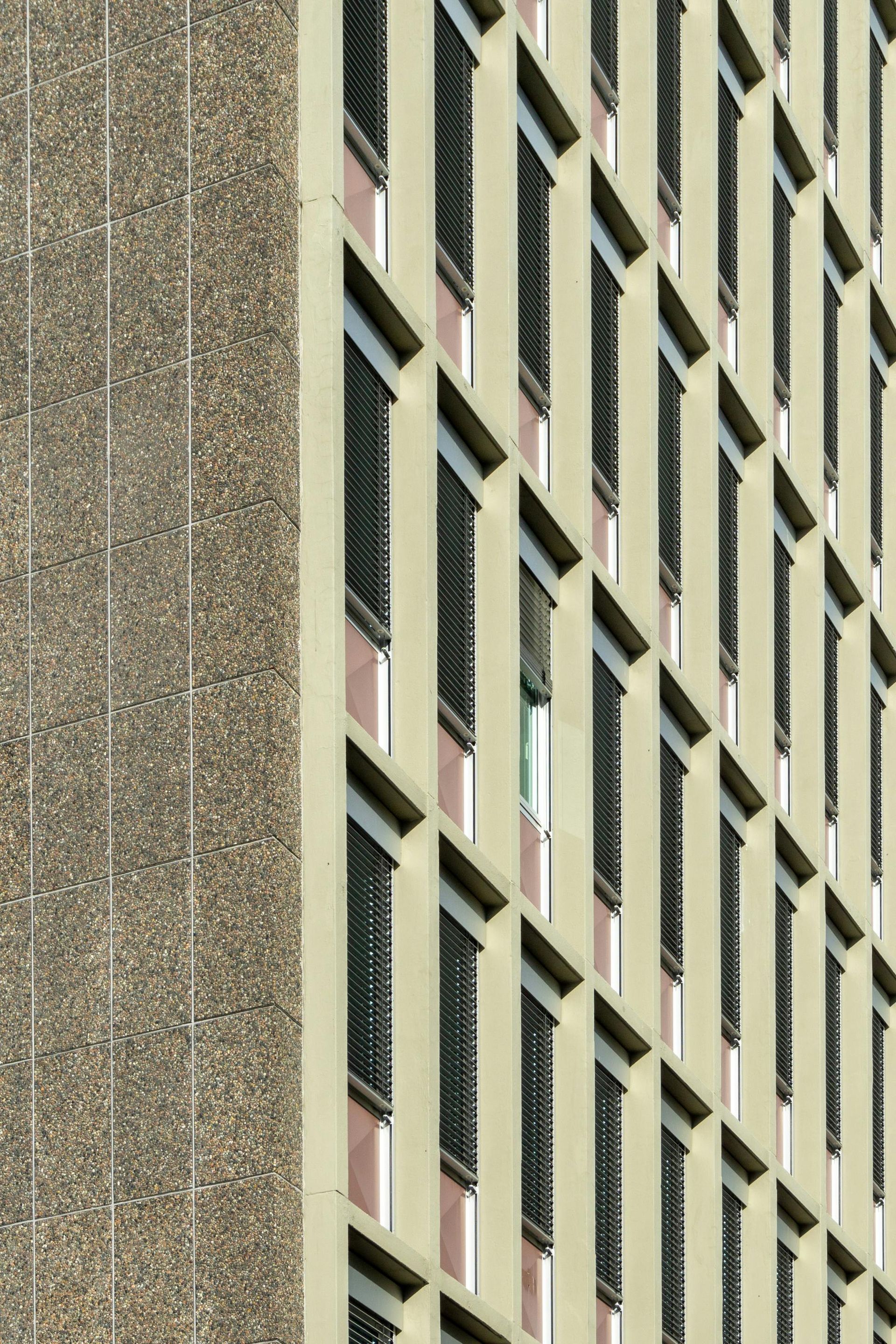 Tan high-rise building with rows of windows, one side covered in textured concrete.
