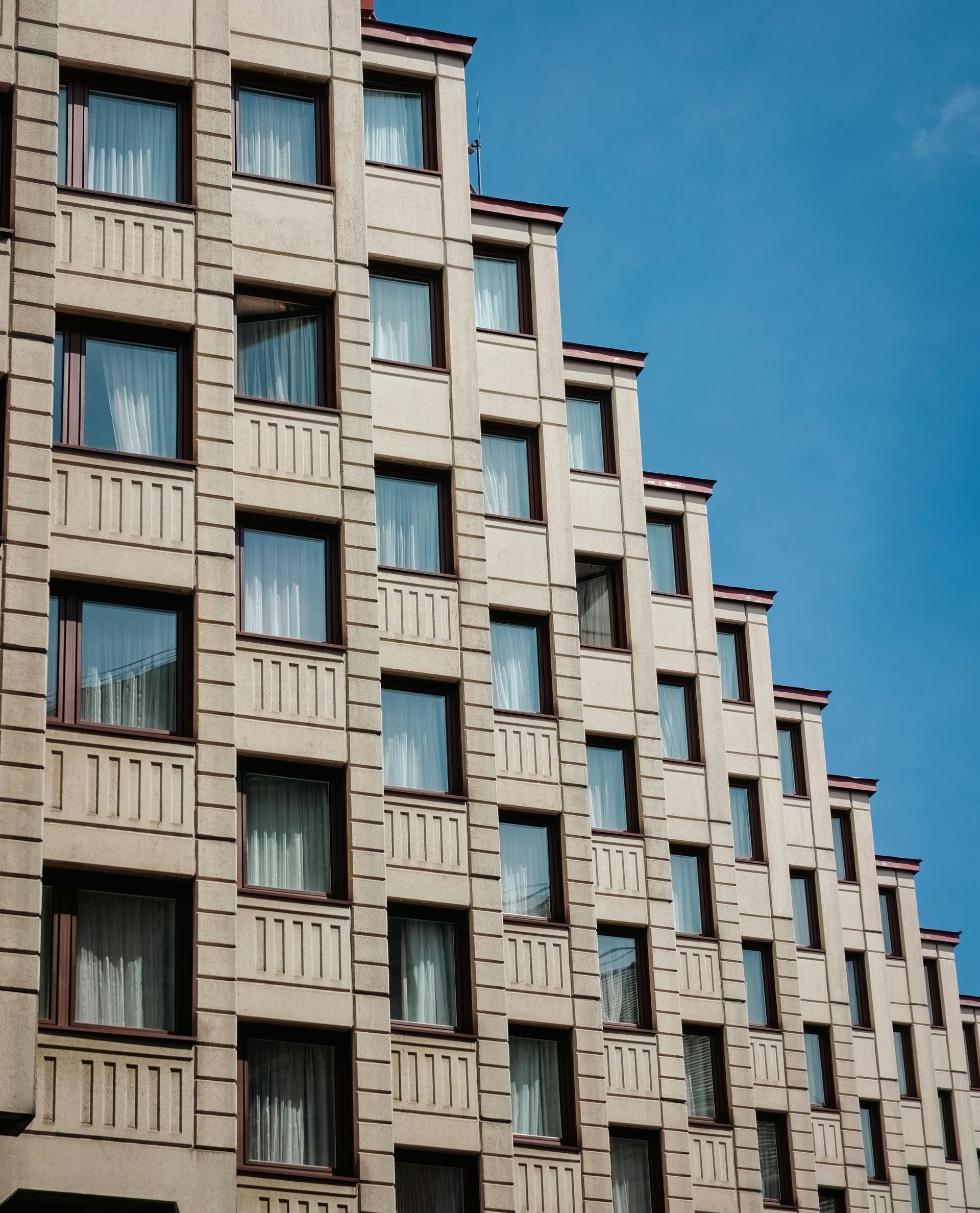 Beige apartment building with stepped facade against a bright blue sky.