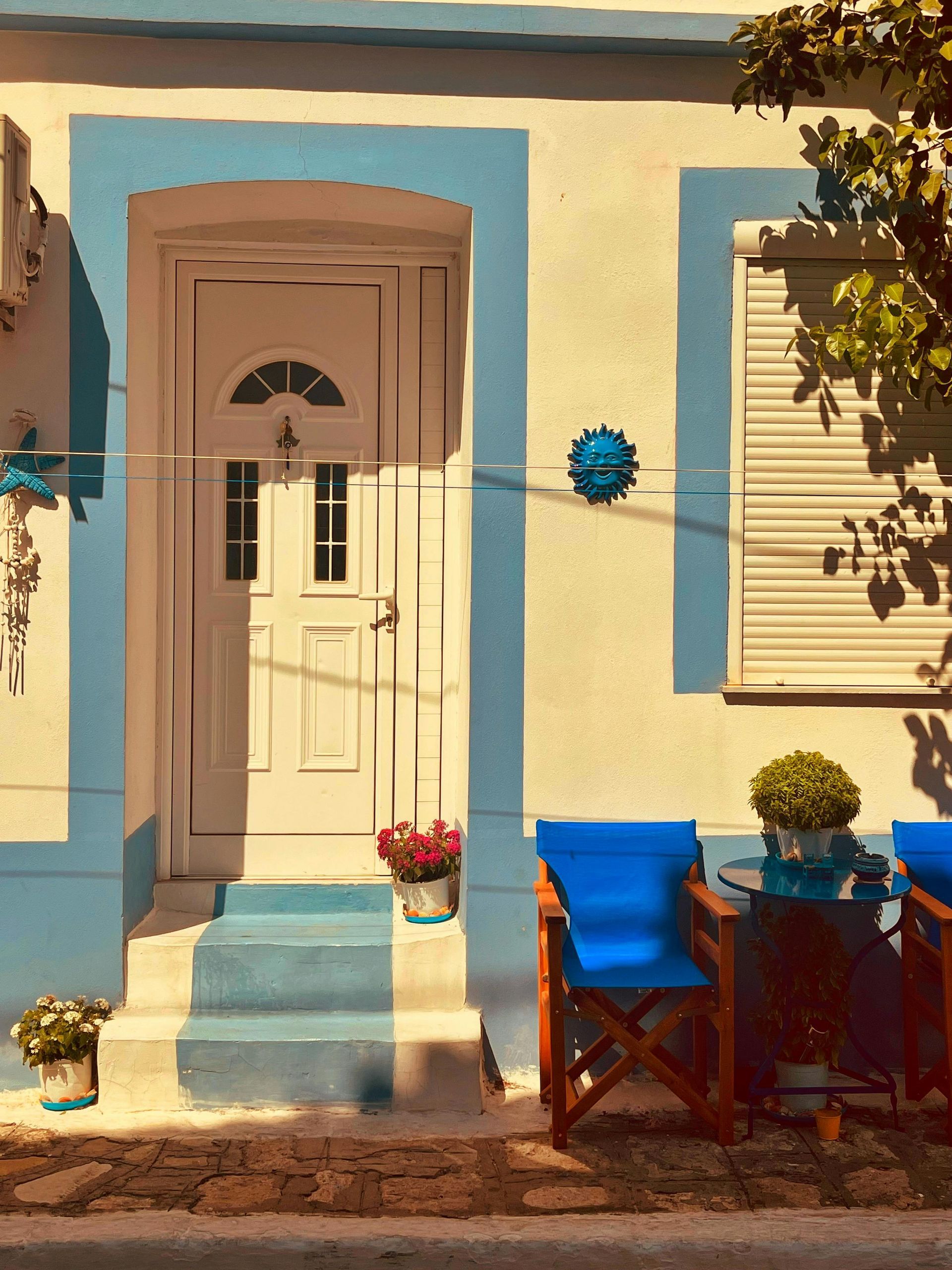 White door with blue trim on a building. Blue chairs and table outside.
