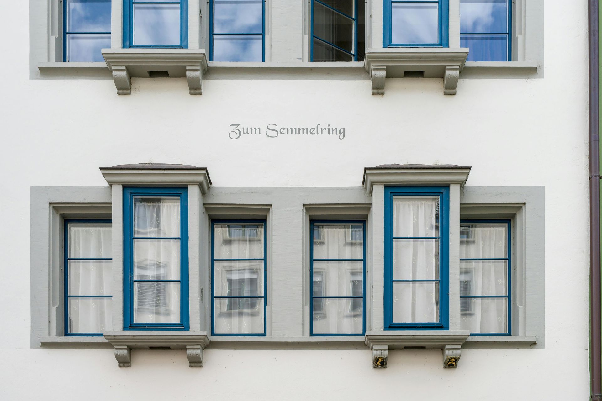 White building facade with blue-framed windows and decorative stone elements.