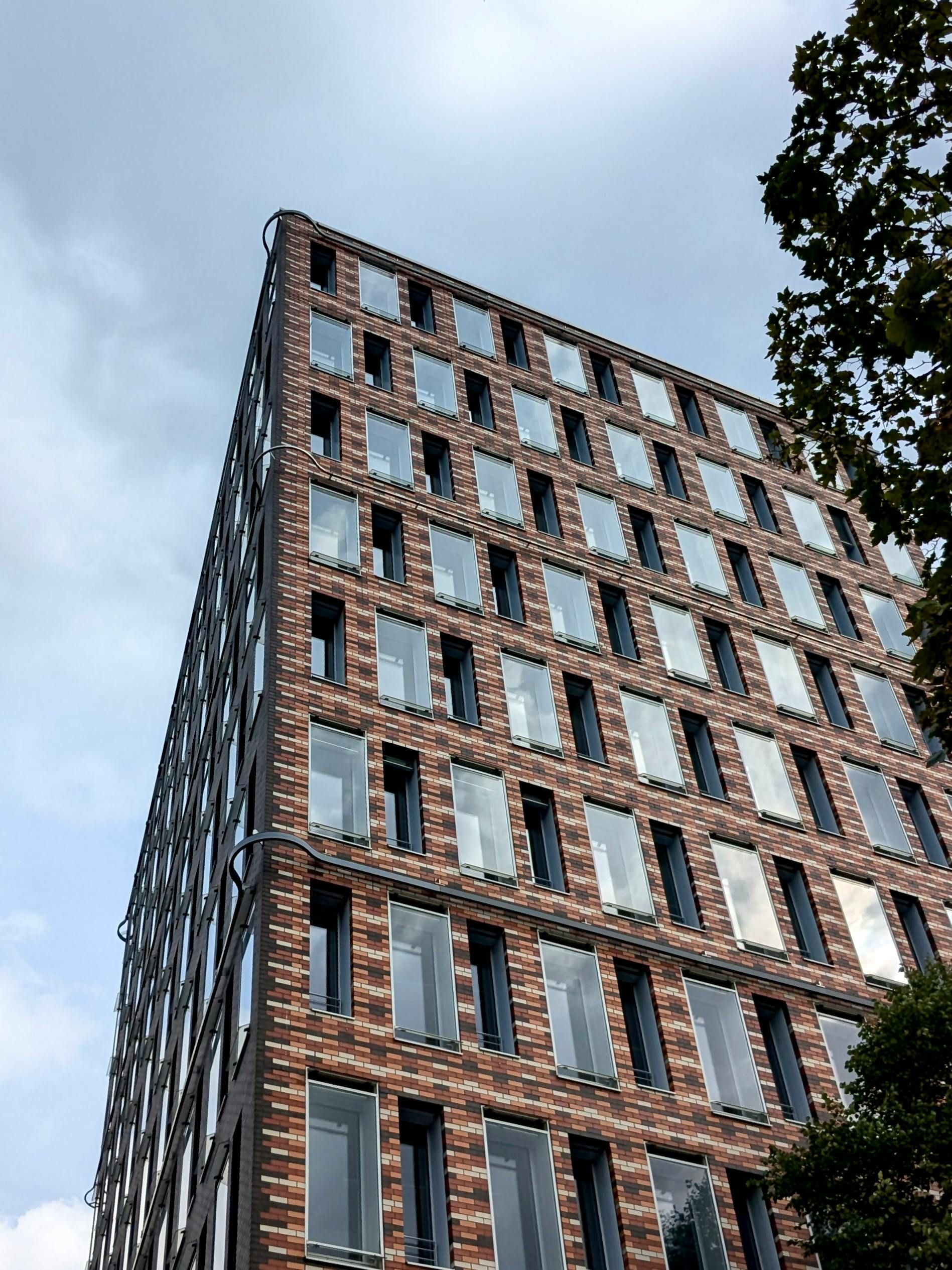 Beige building under a cloudy sky. Sunshine filters through leaves, illuminating the structure on a city street.