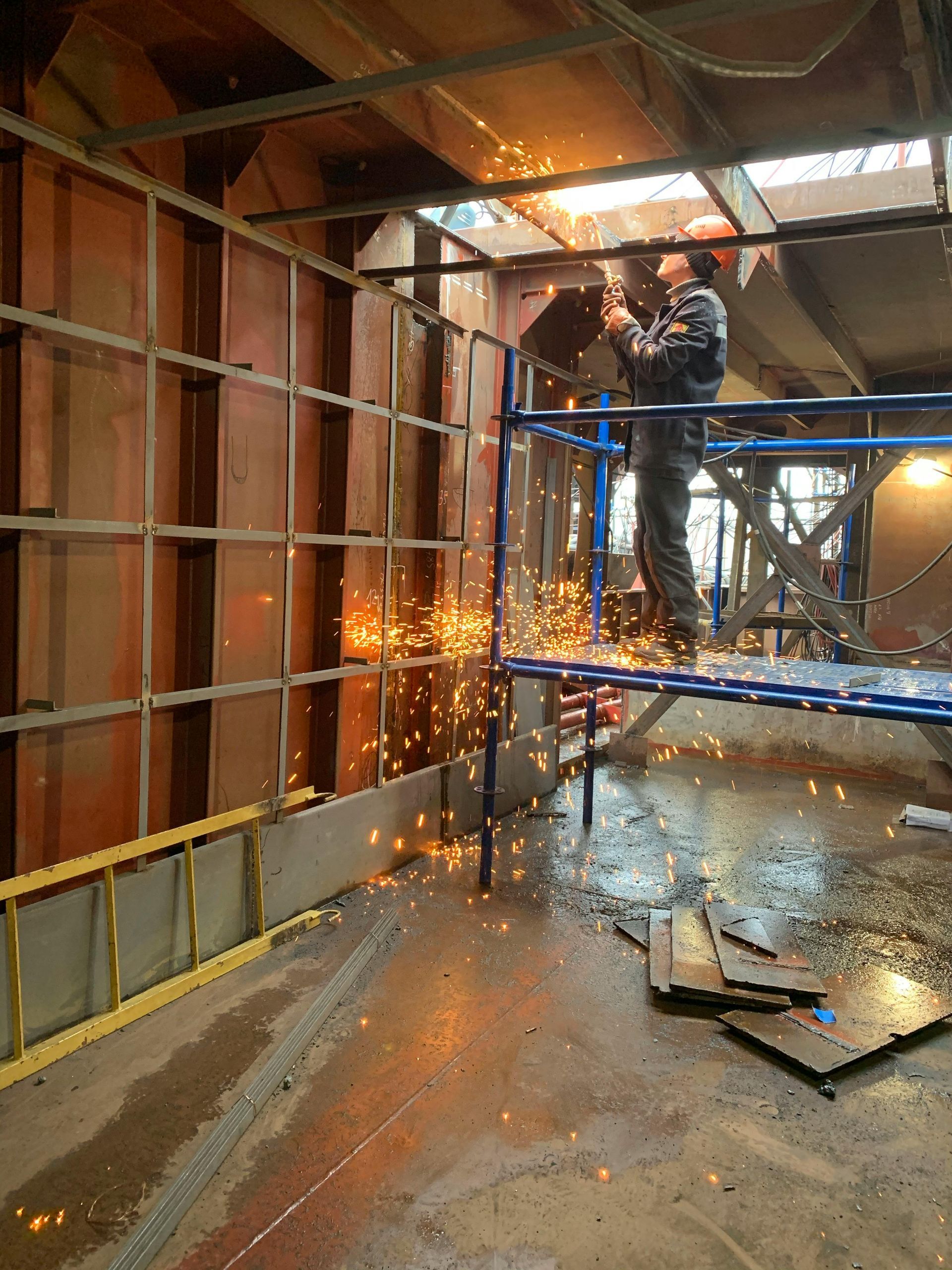 Worker welding metal framework inside a building, creating sparks.