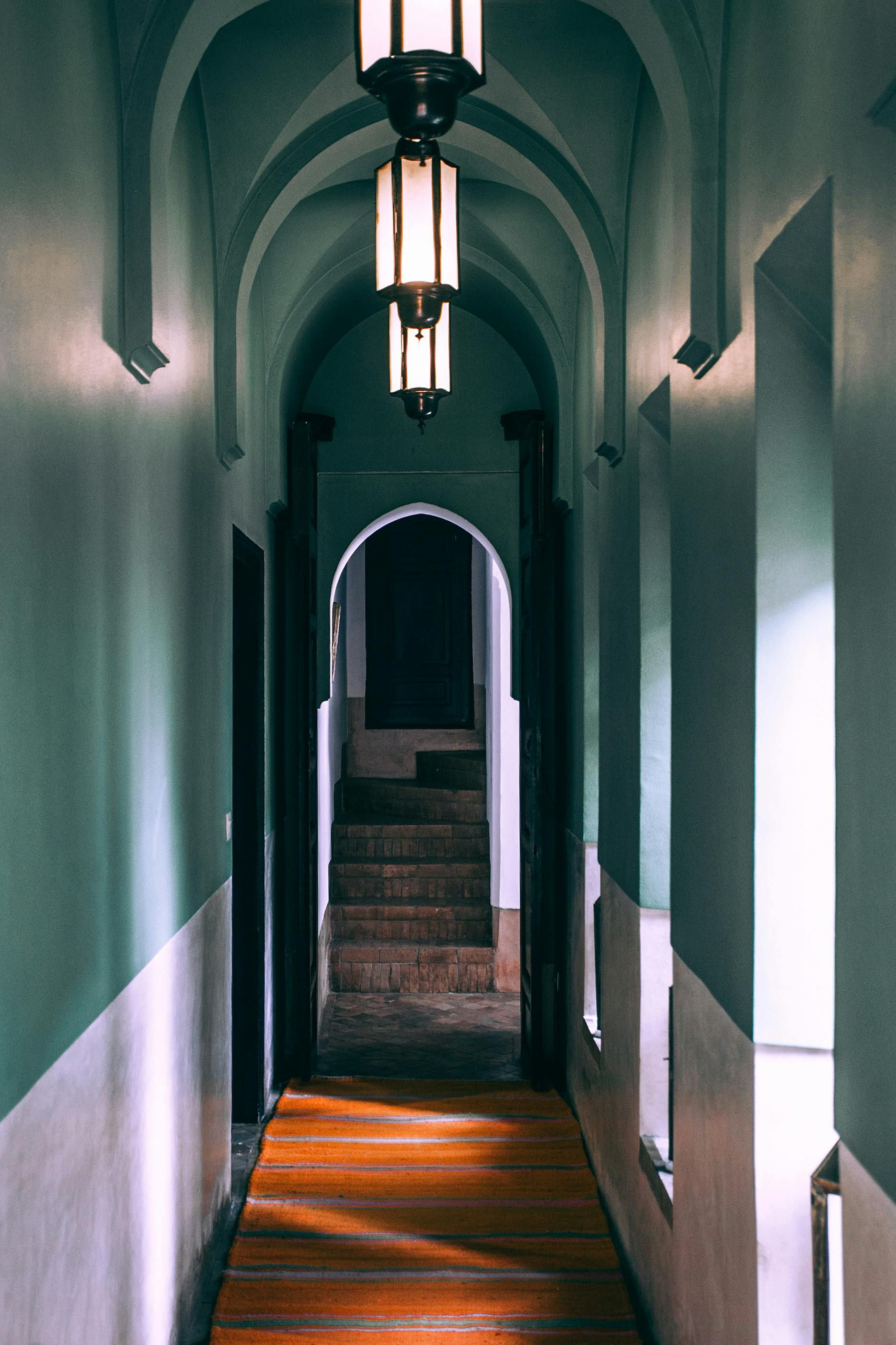 Hallway with arched ceiling, pendant lights, staircase at end, teal and white walls, sunlight.