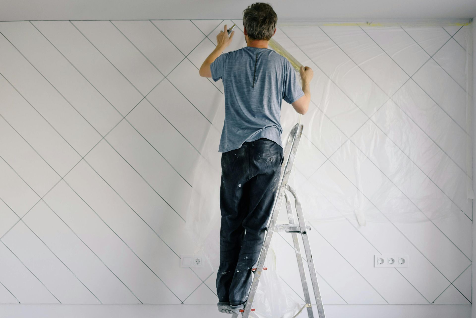 Person on a ladder applying something to a white diagonal-lined wall.