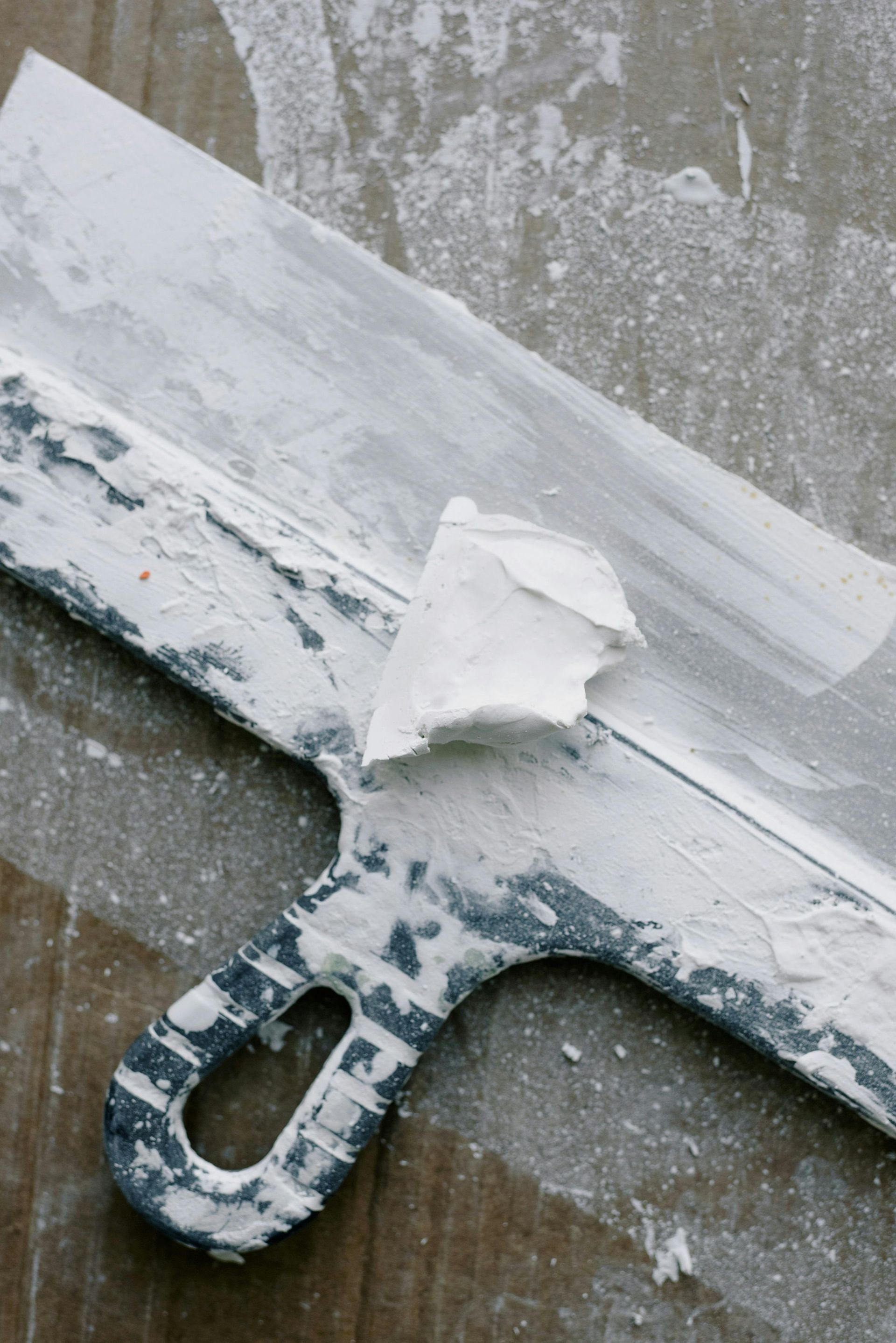 Putty knife covered in white plaster, resting on a wooden surface.