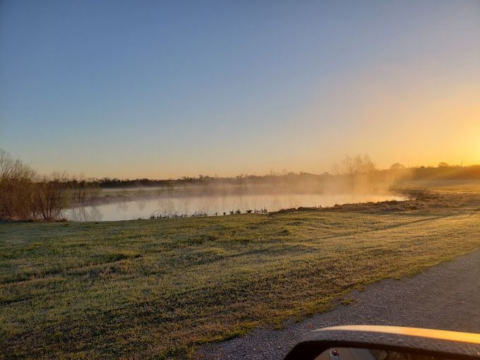 A car is driving down a road next to a lake at sunset.