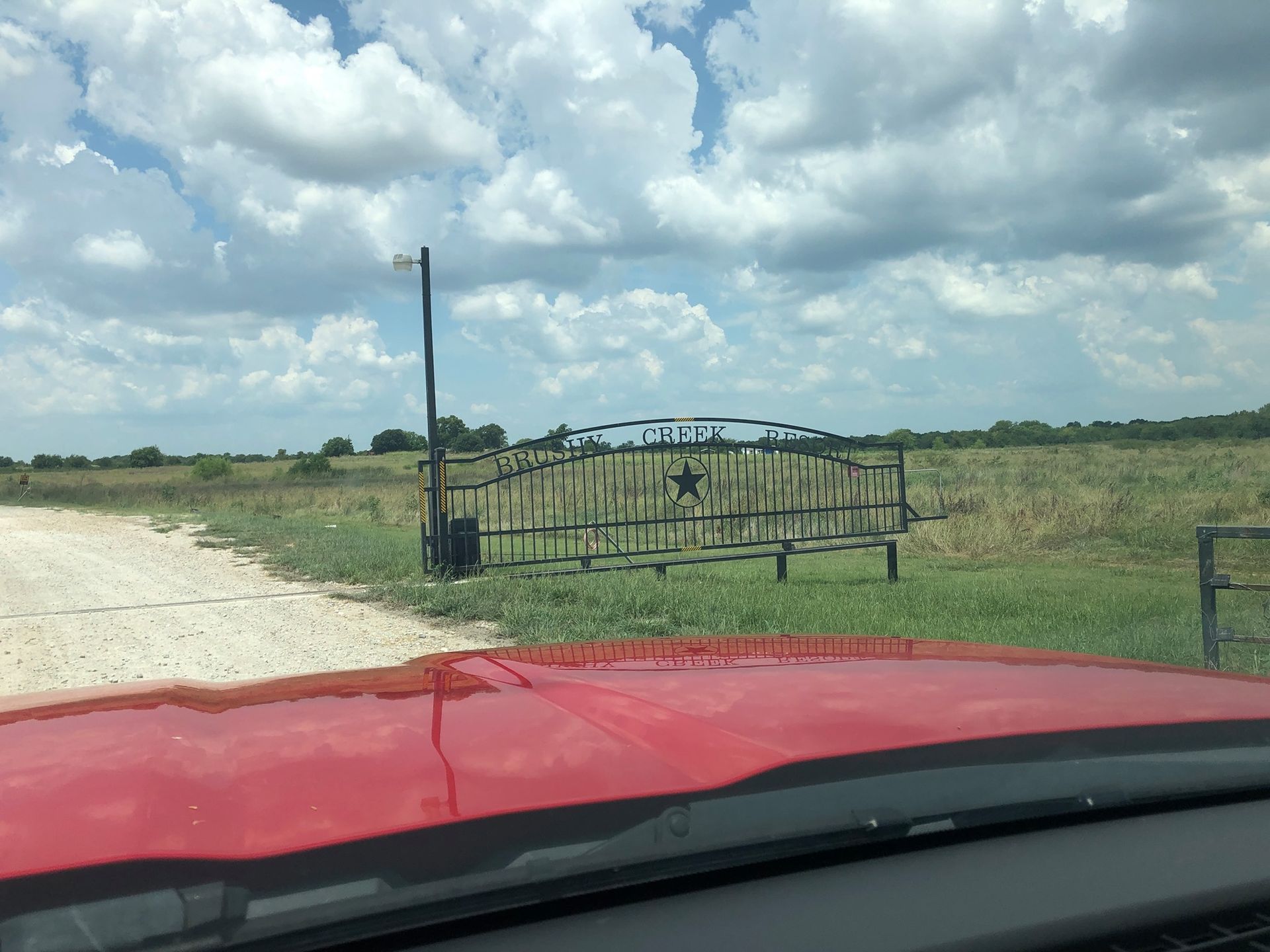 A red truck is driving down a dirt road next to a gate.