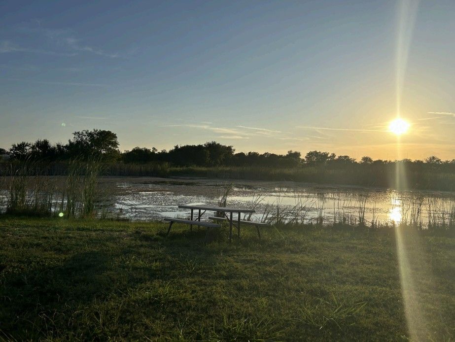 Sunset over a lake with a picnic table on the grassy bank.
