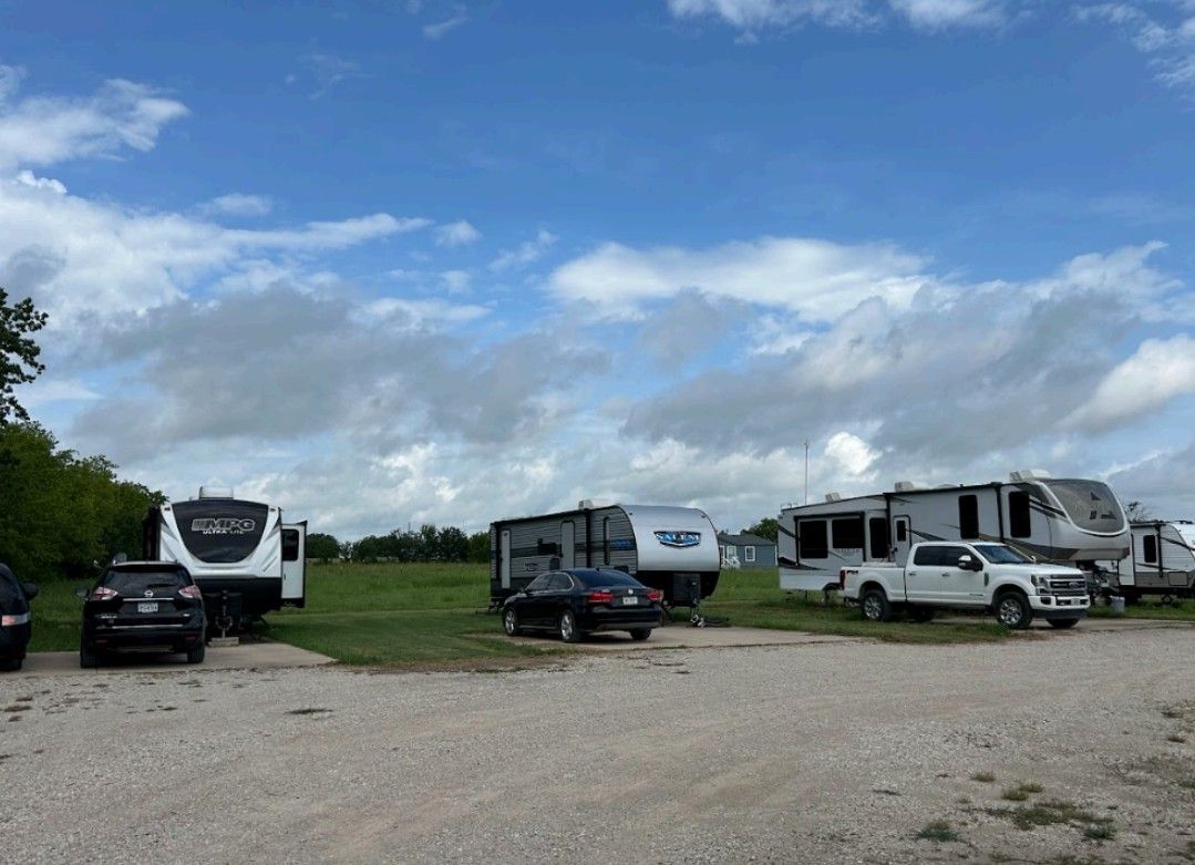 RVs parked in a grassy field with a blue sky and scattered clouds overhead.