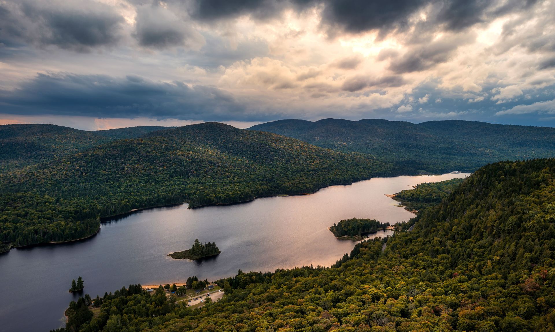 Lake surrounded by green forest under a cloudy sky.