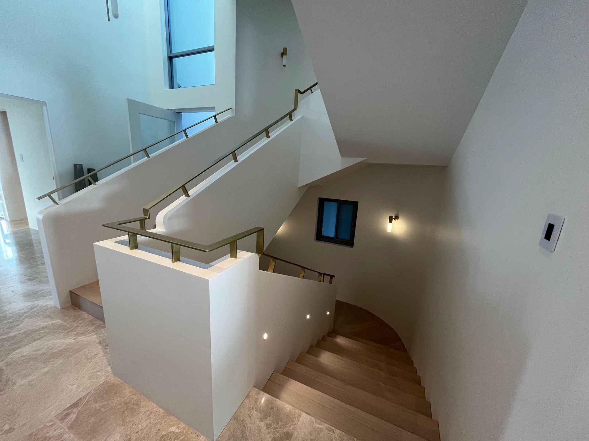 Modern indoor staircase with wooden treads, white walls, gold railings, and small recessed lights along the wall.