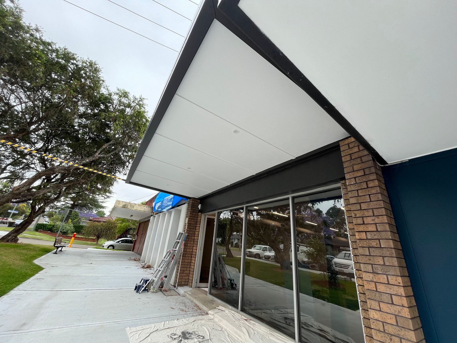 A storefront entrance featuring a large white awning, a dark brick pillar, and a blue wall under a cloudy sky.