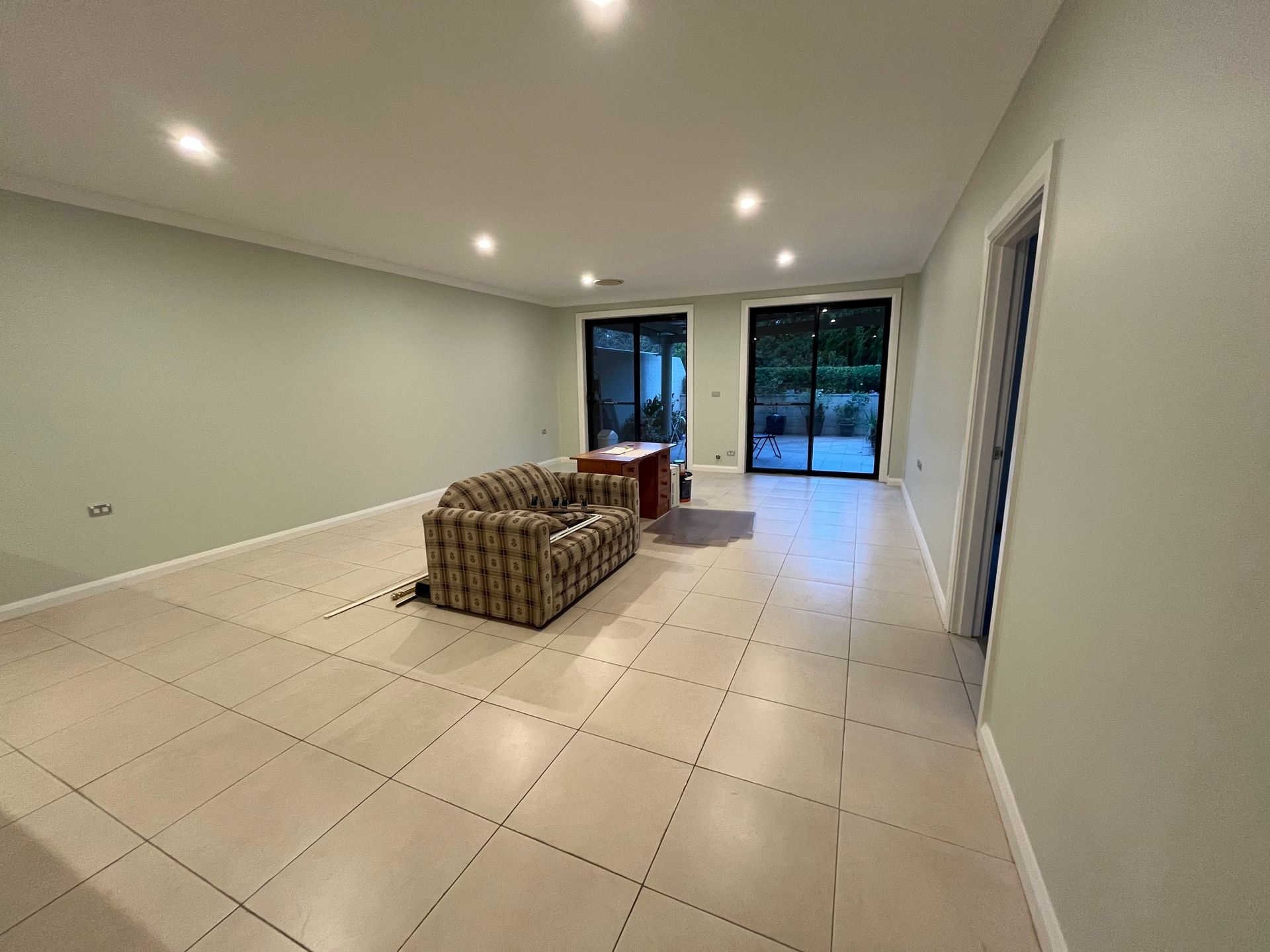 A spacious, bright room with light-colored tile floors, a patterned sofa in the center, and large glass sliding doors.
