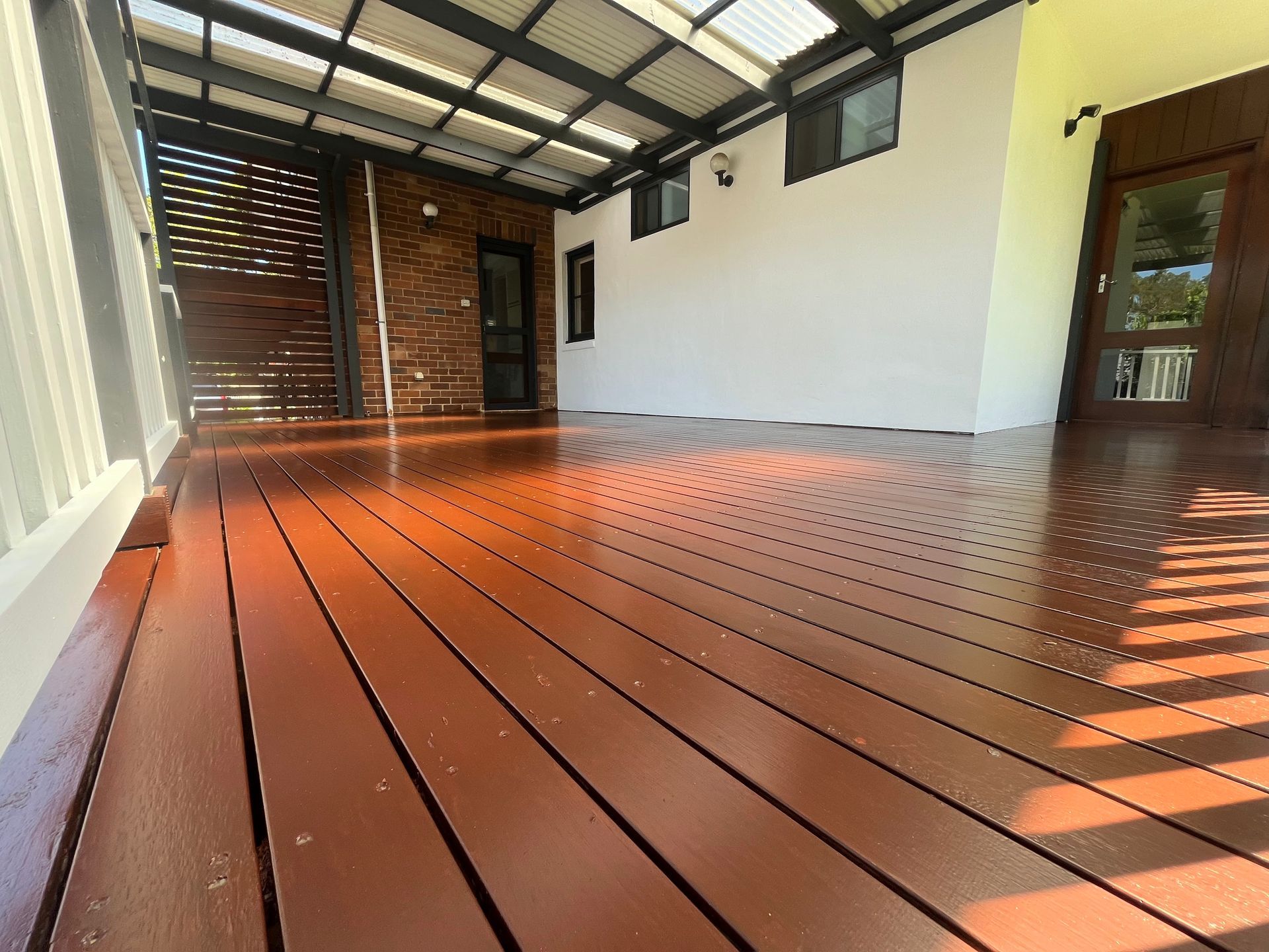 An octagonal gazebo with a dark red shingled roof, cream trim, and dark green posts, situated in a green park.