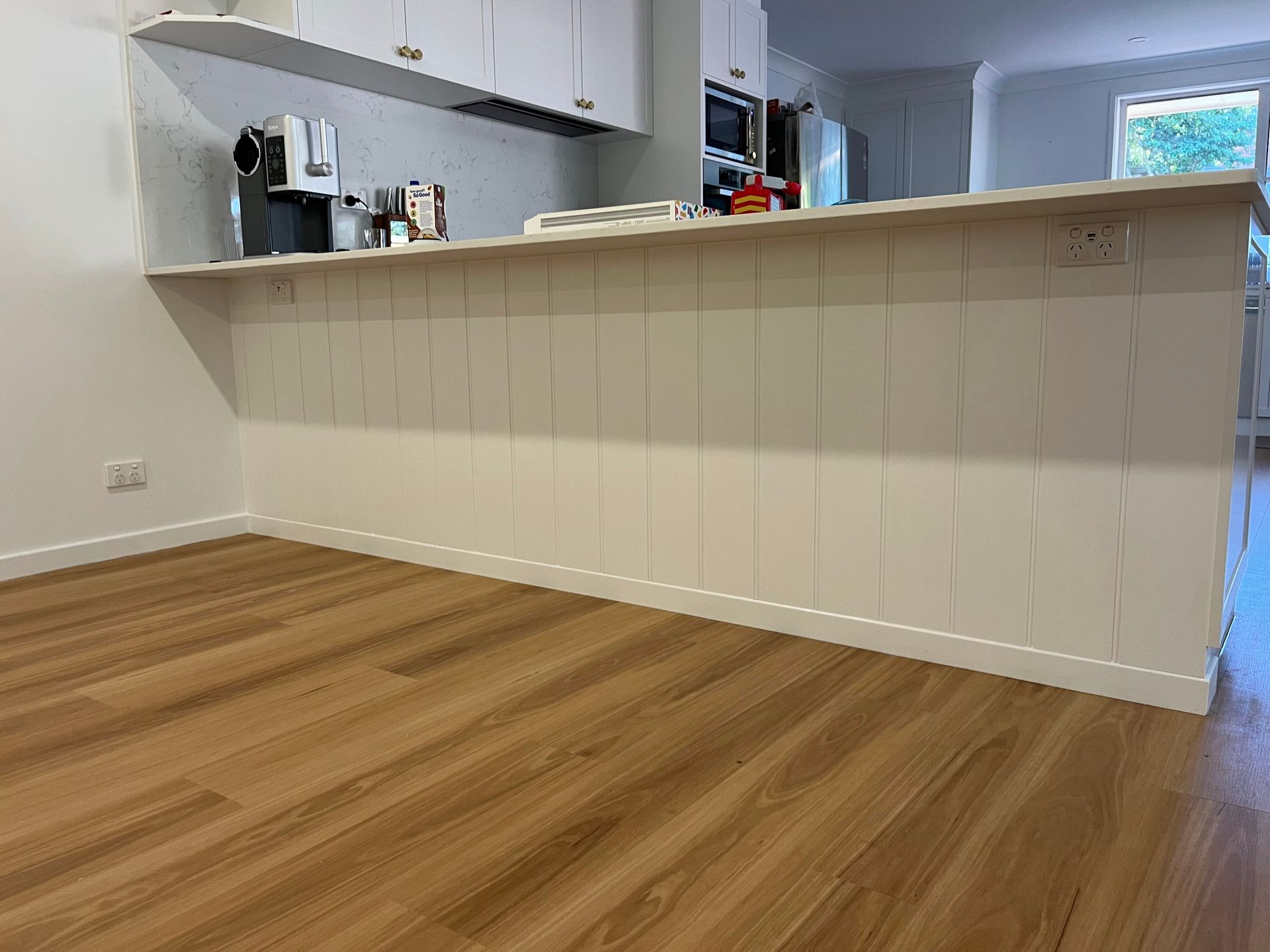 A kitchen island with white vertical paneling and a countertop, set against a wooden floor.
